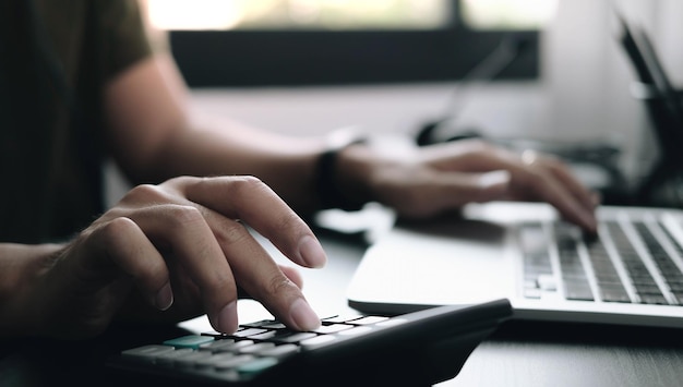 Foto empreendedor em close-up usando calculadora e laptop para fazer finanças matemáticas em uma mesa de madeira no escritório
