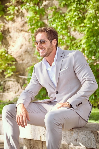 Empreendedor masculino confiante em terno elegante sentado no banco do parque e desviando o olhar no verão