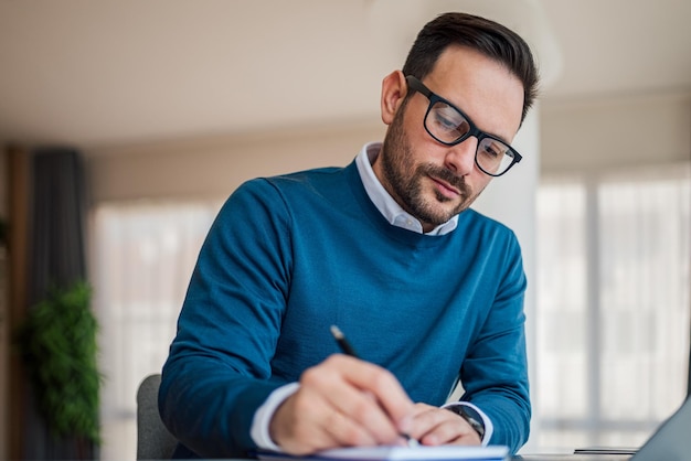 Empreendedor masculino sério escrevendo plano de negócios enquanto trabalhava na mesa do escritório
