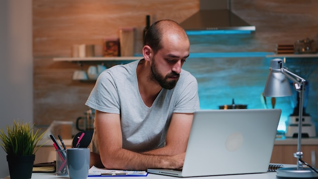 Empreendedor sentado no escritório remotamente, trabalhando no computador laptop, segurando a cabeça com as mãos, olhando para baixo. Funcionário ocupado usando rede de tecnologia moderna sem fio fazendo horas extras para leitura de trabalho