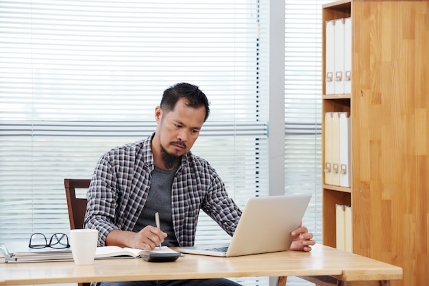 Empreendedor sério lendo e-mail no laptop e assinando documentos e contratos