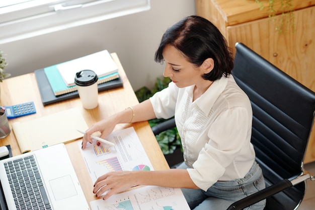 Empreendedora analisando relatório de vendas com vários gráficos e diagramas na mesa à sua frente