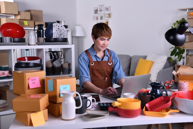 Empreendedora asiática madura, proprietária de uma empresa trabalhando em um laptop, verificando o endereço e os detalhes da entrega antes de enviar o produto ao cliente, quando trabalha em casa