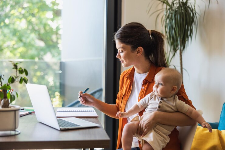 Foto empreendedora feminina escrevendo notas enquanto trabalhava no laptop e cuidava de seu bebê em casa.