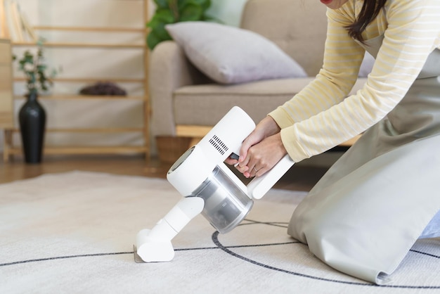 Empregada aspirando no tapete com aspirador de mão sem fio para limpar a poeira na sala de estar