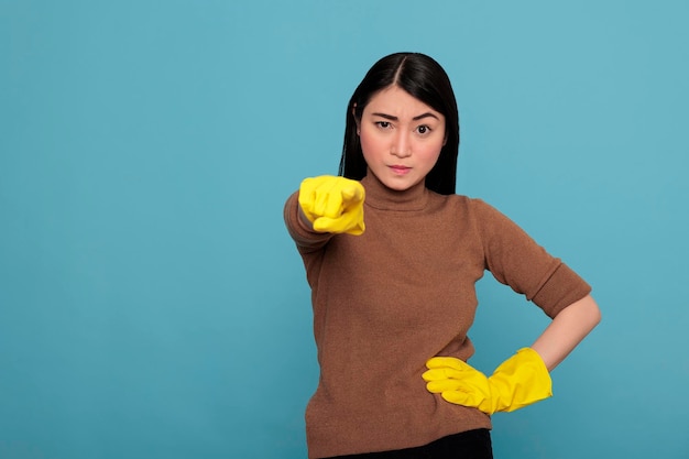 Empregada de casa asiática triste e exausta com raiva no trabalho usando luvas amarelas apontando o dedo para a frente, conceito de limpeza em casa, mulher infeliz estressada com estado de espírito negativo