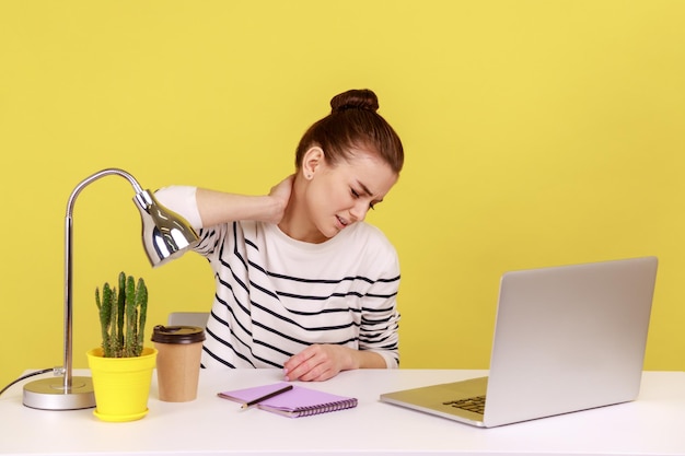 Empregada de escritório sobrecarregada sentada à mesa e trabalhando no laptop sente dor no pescoço