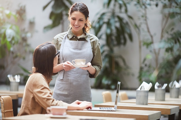 Empregada de mesa bonita que dá a xícara de café ao cliente