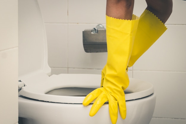 Empregada doméstica usando luvas de borracha amarela e usando escova de limpeza no banheiro