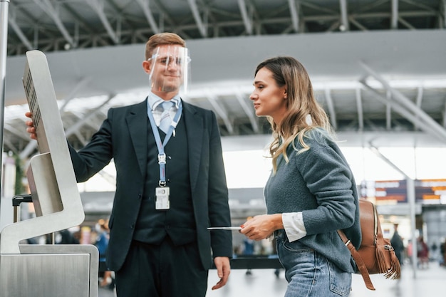 Empregado ajudando a usar o terminal Jovem turista está no aeroporto durante o dia