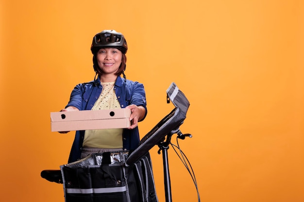 Empregado de entrega sênior entregando comida para viagem em caixa de papelão para o cliente, usando bicicleta como transporte de trabalho. Trabalhador de restaurante vestindo camiseta azul e boné enquanto trabalhava como mensageiro