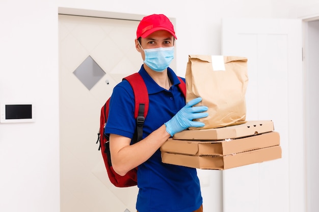 Empregado de entregador em luvas de máscara uniforme de t-shirt de boné vermelho dar caixas de pizza de pedido de comida isoladas no estúdio de fundo amarelo. Serviço quarentena pandêmica coronavírus vírus influenza conceito 2019-ncov