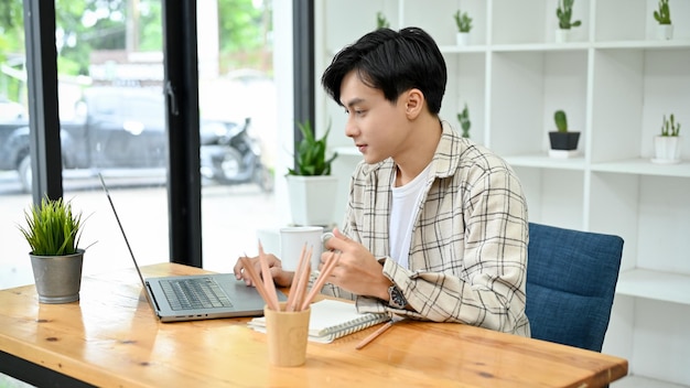 Empregado de escritório masculino asiático inteligente e profissional usando laptop enquanto toma café