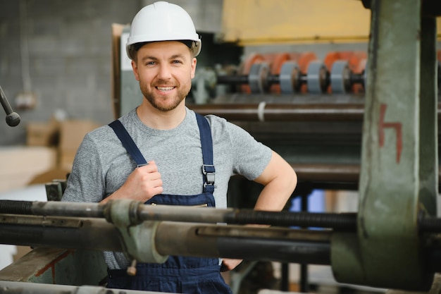 Empregado sorridente e feliz trabalhador industrial dentro de casa na fábrica jovem técnico com capacete branco