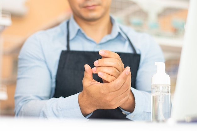 Empregado usando álcool gel para limpar as mãos para trabalhar em uma cafeteria