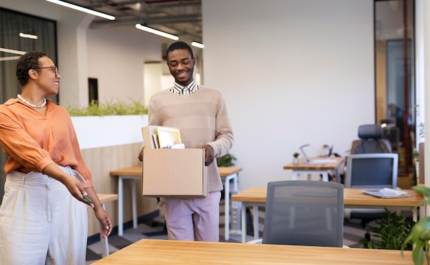 Empregador mostrando ao homem sua mesa em um novo emprego enquanto carrega a caixa de pertences