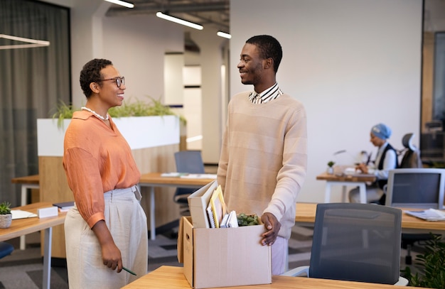 Empregador mostrando ao homem sua mesa em um novo emprego enquanto carrega a caixa de pertences