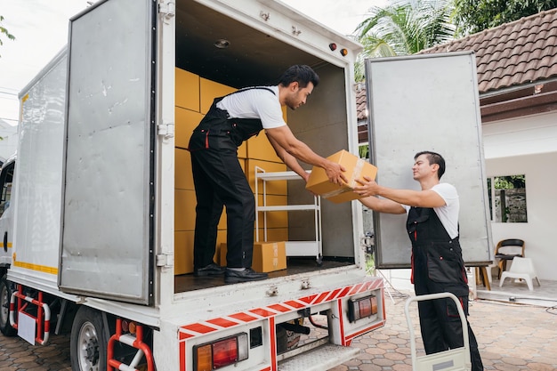 Empregados em uniforme trabalham juntos para descarregar caixas do caminhão de mudança para a realocação do cliente A dedicação da empresa garante uma mudança feliz Dia de mudança