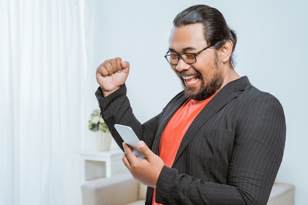 Emprendedor emocionado levanta su brazo gesto de éxito con el teléfono