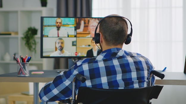 Emprendedor inmovilizado en silla de ruedas hablando con su equipo mediante auriculares durante una videollamada.