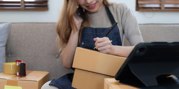 Emprendedor de pequeñas empresas de una mujer asiática independiente que usa una computadora portátil con una caja Caja de embalaje de marketing en línea de éxito alegre y concepto de idea de PYME de entrega