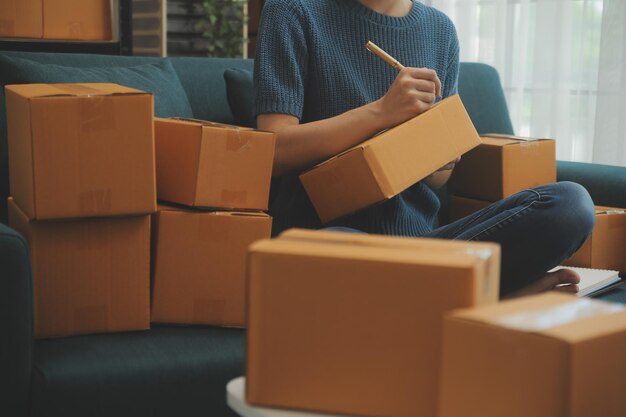 Emprendedor de pequeñas empresas o mujer asiática independiente que usa una computadora portátil con caja Mujer asiática de éxito joven con su mano levanta la caja de embalaje de marketing en línea y el concepto de PYME de entrega