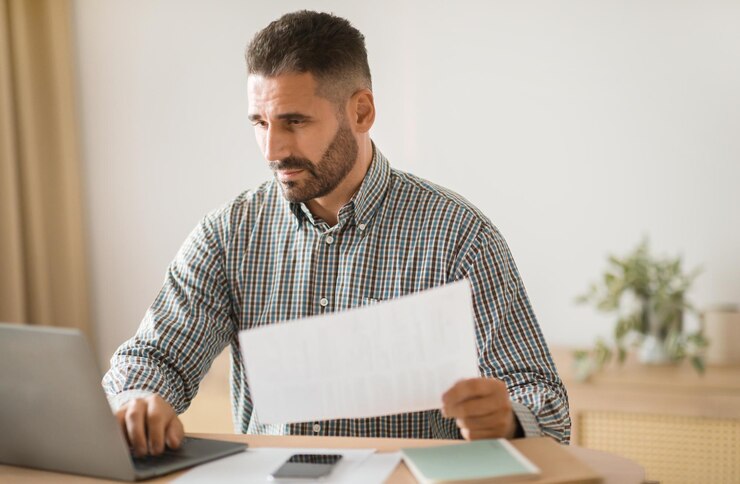 Emprendedor revisando el papel y navegando en la computadora portátil en una oficina moderna
