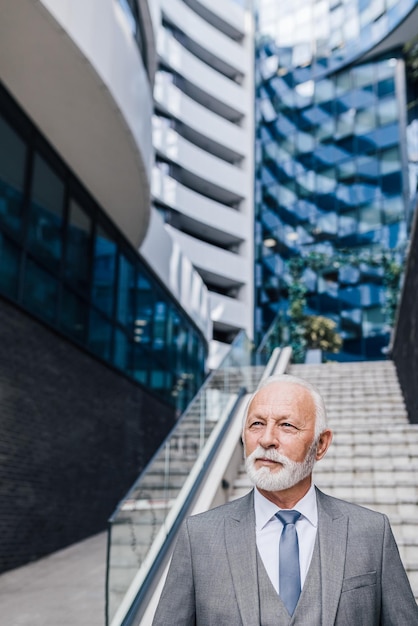 Emprendedor serio y reflexivo que mira hacia otro lado mientras está parado fuera del edificio de negocios