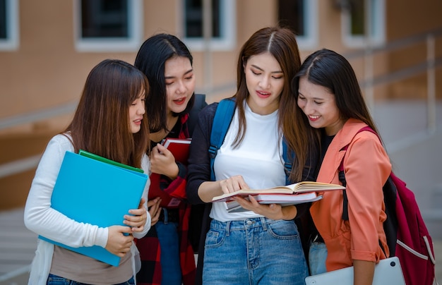 Empresa de alegres alunas asiáticas com cadernos em pé no campus universitário e se juntando com diversão e sentimento íntimo. Amigo próximo no conceito de faculdade.