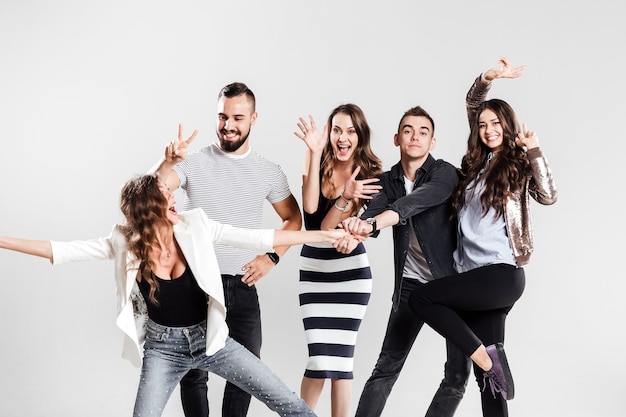 Empresa de garotas e caras vestidos com roupas casuais elegantes estão brincando sobre um fundo branco no estúdio.