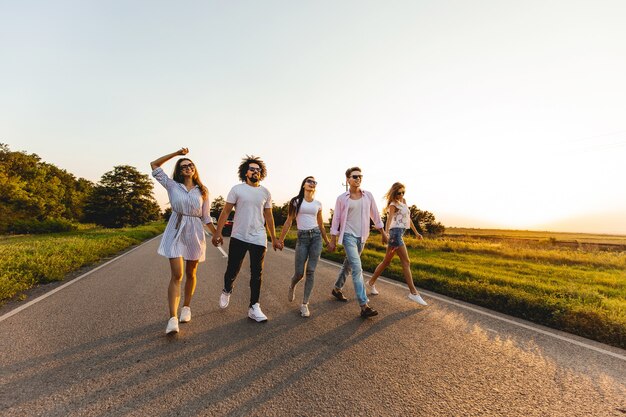 Foto empresa de rapazes elegantes jovens felizes caminhar em uma estrada rural em um dia ensolarado.