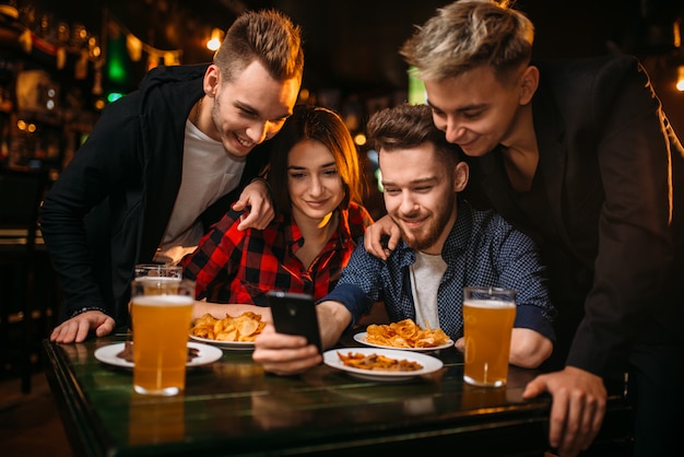 Empresa divertida assiste a foto no telefone em um bar esportivo, fãs de futebol felizes