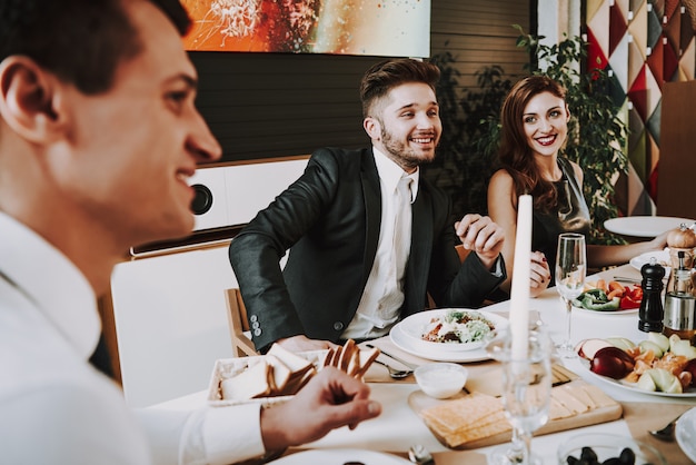 Empresa joven se sienta en trajes alrededor de la mesa de la cena.