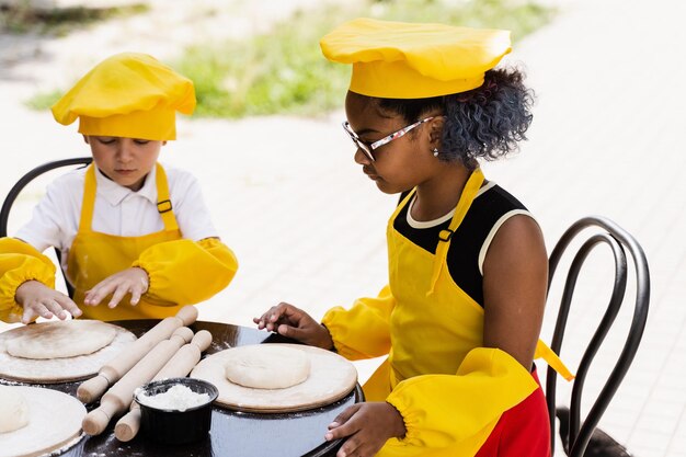 Empresa multinacional de crianças cozinha em uniformes amarelos cozinhando massa para padaria Adolescente africano e garota negra se divertem com menino caucasiano e cozinham comida