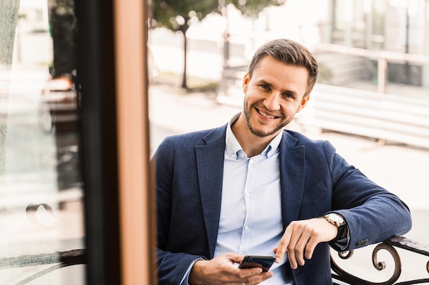 La empresa trabaja en línea mediante el teléfono. Trabajo remoto. Hombre guapo en café en la terraza de verano.