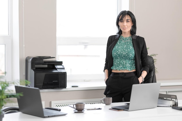 Empresária adulta no escritório de terno em pé na área de trabalho com laptop