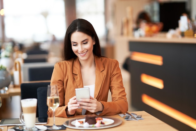 La empresaria adulta con smartphone en el almuerzo en el café