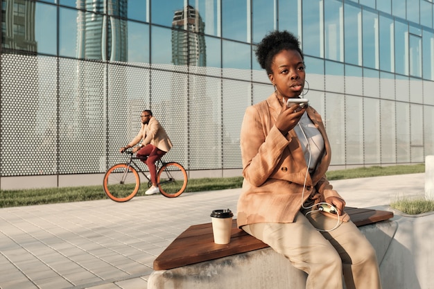 Empresaria africana hablando por teléfono móvil y tomando café durante su pausa para el café en la ciudad