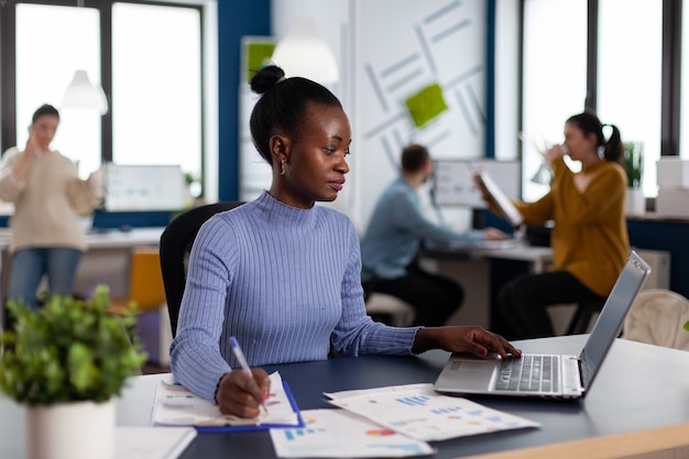 La empresaria africana tomando notas en el portapapeles analizando estadísticas en la oficina de puesta en marcha