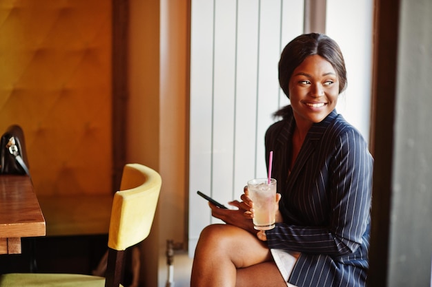 Empresária afro-americana bebendo coquetel limonada no café Garota negra descansando com telefone celular
