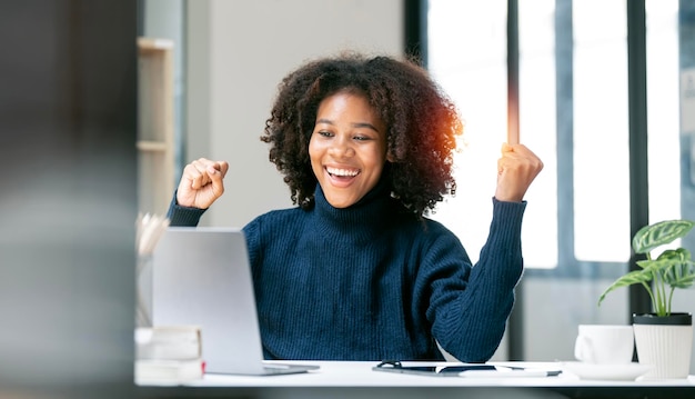 Empresária afro-americana bem-sucedida e emocionante, animada para vencer em seu laptop no trabalho