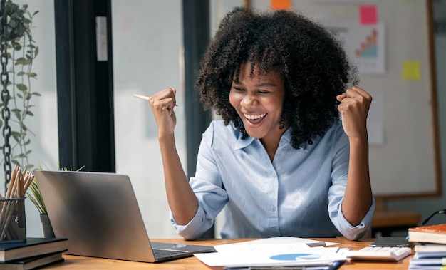 Empresária afro-americana bem-sucedida e empolgante, animada para vencer em seu laptop no trabalho