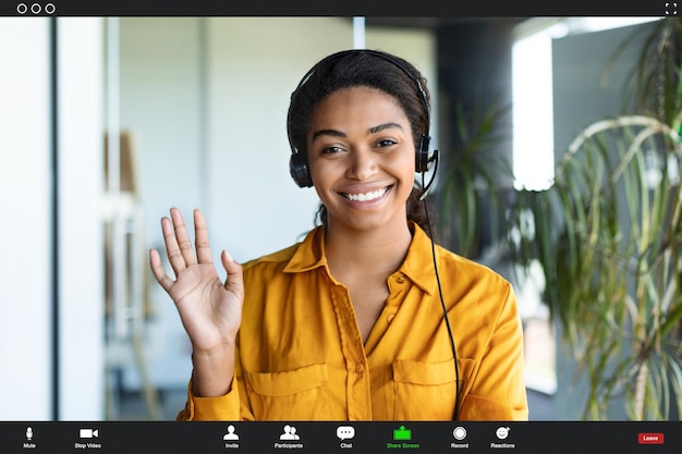 Foto empresária afro-americana positiva fazendo videochamada do escritório acenando com a mão para a câmera e sorrindo captura de tela do pov
