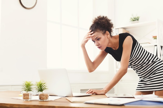 Empresaria afroamericana sorprendida en la oficina moderna. Mujer que trabaja en la computadora portátil en la oficina, espacio de copia