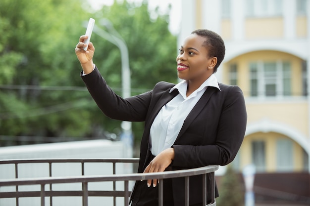 Empresaria afroamericana en traje de oficina sonriendo, parece segura y feliz, exitosa