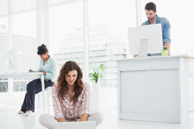 Empresaria alegre que se sienta en el suelo usando la computadora portátil