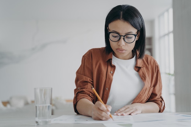 Empresaria con anteojos trabaja en un proyecto empresarial hace notas sentadas en el escritorio del lugar de trabajo en la oficina