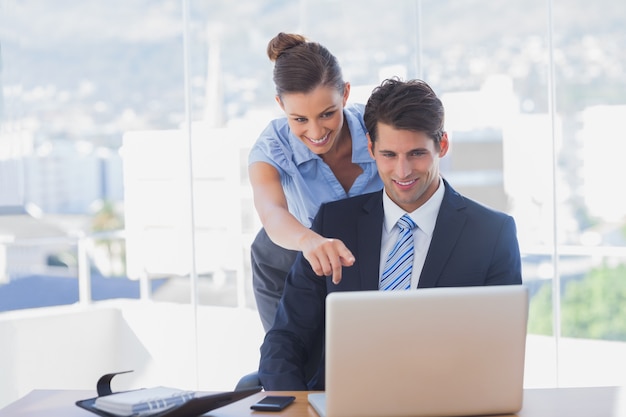 Empresaria apuntando a la computadora portátil y sonriendo en la oficina