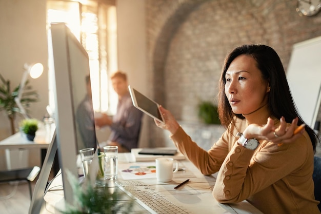 Empresária asiática analisando relatórios no PC desktop enquanto trabalhava no escritório