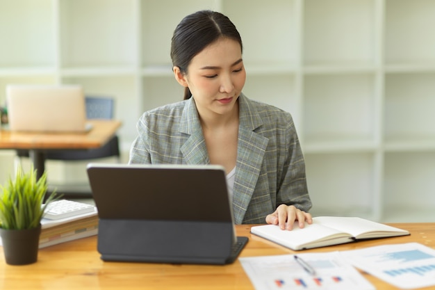 Empresaria asiática analizando estadísticas en tableta trabajando con informes de gráficos gráficos financieros